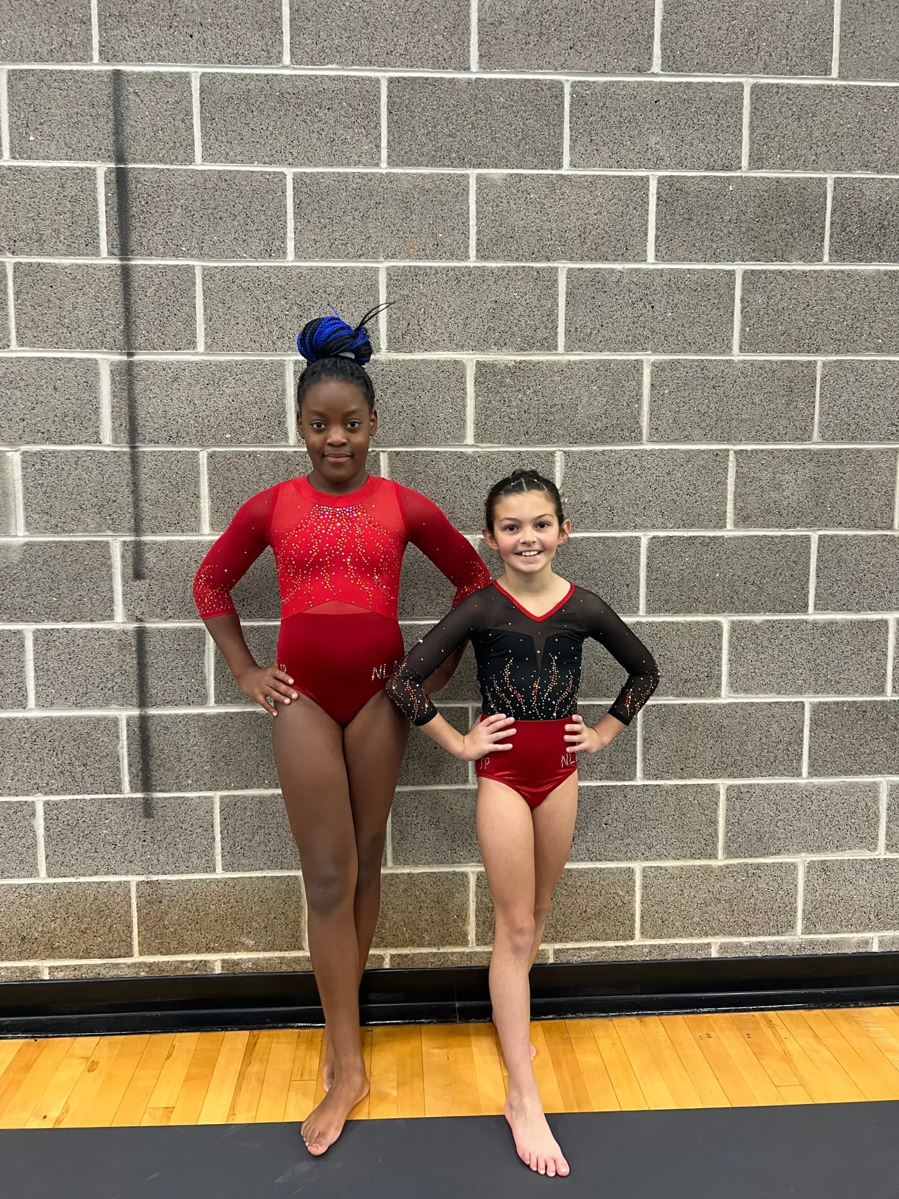 Two Next Level gymnasts in red and black competition leotards