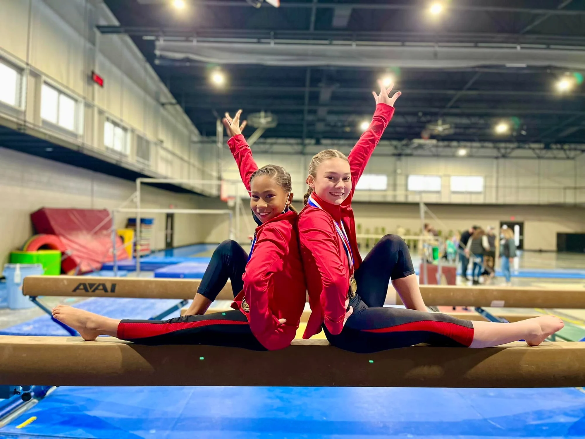 Two Next Level gymnasts holding split poses on a balance beam inside the gym